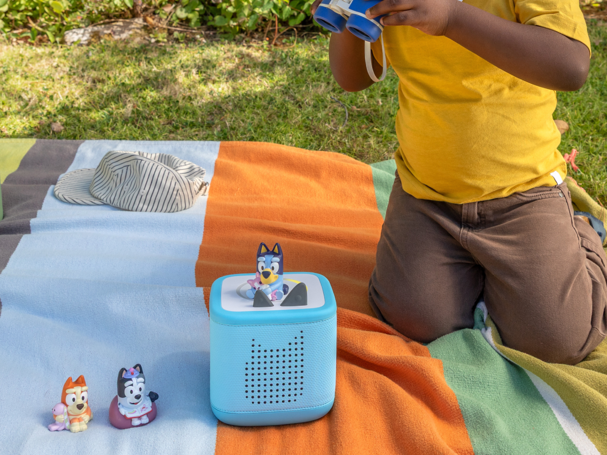 child playing with a blue toniebox 2 and three Bluey Tonies outside
